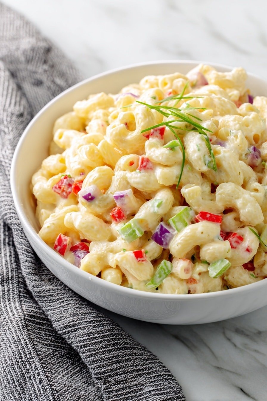 A white bowl filled with a creamy macaroni salad, made of soft elbow-shaped pasta coated in a thick, pale yellow sauce. Mixed through the salad are small, colorful pieces of diced red bell pepper, green celery, and tiny bits of purple onion. Light green herb sprigs are scattered on top, adding fresh detail. The bowl sits on a white marbled surface with a gray and white striped cloth nearby. Photo taken with an iphone --ar 2:3 --v 7 — Dolly Parton’s Macaroni Salad, easy macaroni salad recipe, summer pasta salad, creamy macaroni salad, Southern-style pasta salad