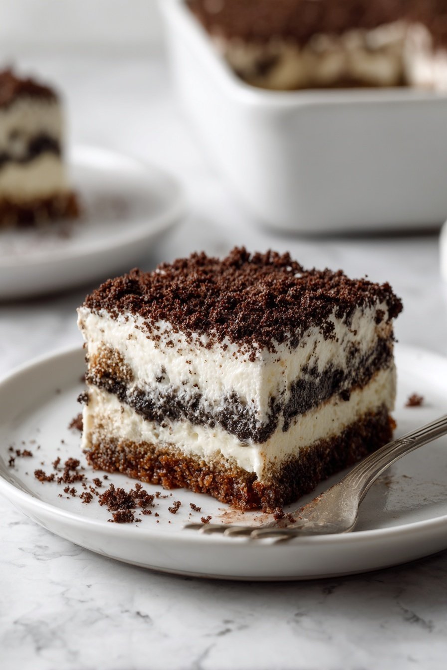 A square piece of dessert sits on a white plate on a white marbled surface. The dessert has three layers: a bottom layer of dark chocolate cake, a thick middle layer of white creamy filling, and a top layer of dark chocolate crumbs. A fork with a small bite of the dessert on its tips lies on the plate near the piece, showing the texture of the three layers. In the background, a larger glass dish with more of the same dessert is slightly blurred. Photo taken with an iphone --ar 2:3 --v 7 — Easy Oreo Dirt Cake, Oreo Dirt Cake recipe, no-bake Oreo dessert, chocolate Oreo pudding, quick Oreo dirt cake