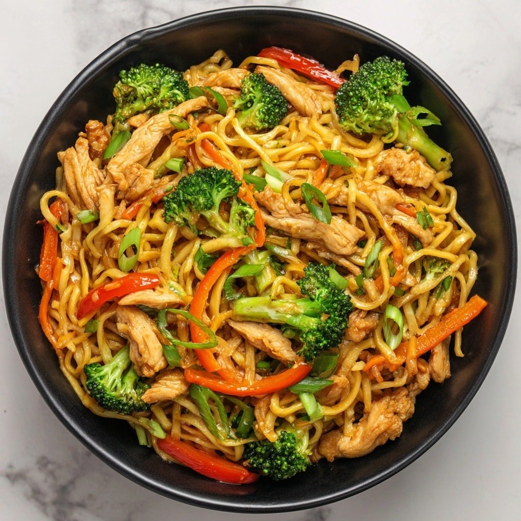 A close-up of a black bowl filled with stir-fried noodles mixed with bright green broccoli pieces, thinly sliced red bell peppers, and carrot strips. The noodles have a shiny, light brown sauce coating, and there are several pieces of light golden brown cooked chicken layered throughout. Chopped green onions are sprinkled on top for extra color and freshness. The bowl is placed on a white marbled surface. photo taken with an iphone --ar 1:1 --v 7 — One-Pan Chicken Noodles Stir-Fry, quick chicken noodle stir-fry, easy Asian-inspired dinner, healthy chicken stir-fry recipe, simple weeknight stir-fry