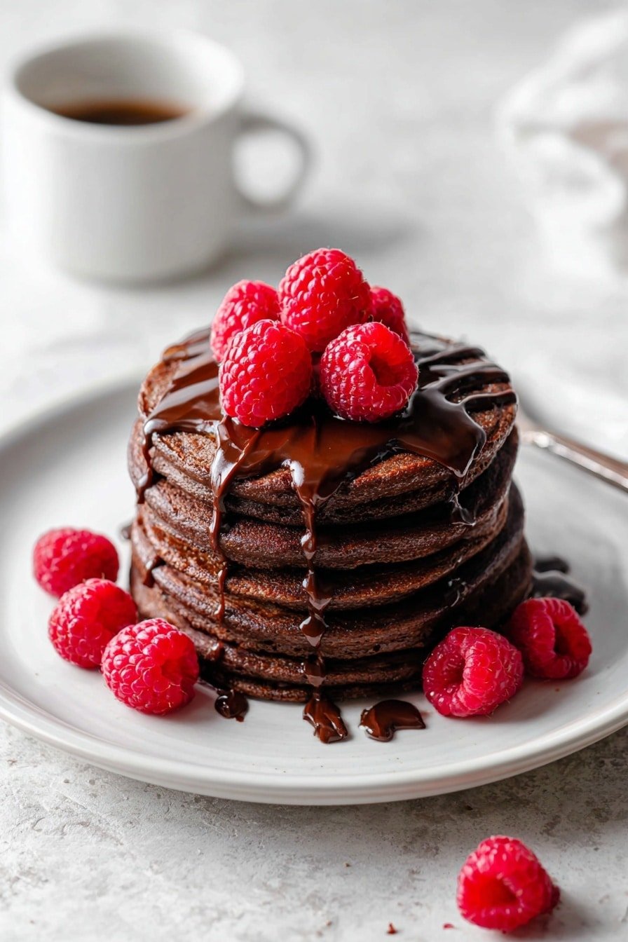 A stack of five round, thick chocolate pancakes sits centered on a white plate. Each pancake is dark brown with a soft, slightly textured surface. Chocolate syrup is generously drizzled over the top pancake, running down the sides in shiny, smooth streams, pooling at the base. On top of the stack, there are five bright red raspberries, fresh and plump, with additional raspberries placed around the plate. The plate rests on a white marbled texture surface, and there is a blurred white cup of coffee in the background. photo taken with an iphone --ar 2:3 --v 7 — Chocolate Protein Pancakes, easy healthy breakfast, high-protein pancake recipe, chocolate banana pancakes, quick nutritious breakfast