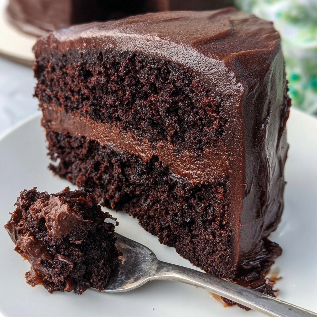 The image shows a thick slice of chocolate cake with two dark brown layers of moist cake separated by a rich, dense dark chocolate frosting layer in the middle. The outside is covered with a smooth, thick layer of the same dark chocolate frosting. The slice is placed on a white plate that rests on a white marbled surface. A silver fork holds a piece of the creamy frosting close to the cake's base. In the background, a woman's hand slightly blurred holds a fork near the plate. Photo taken with an iphone --ar 1:1 --v 7 — Brick Street Chocolate Cake, easy chocolate cake recipe, moist chocolate cake, rich chocolate cake, classic chocolate cake