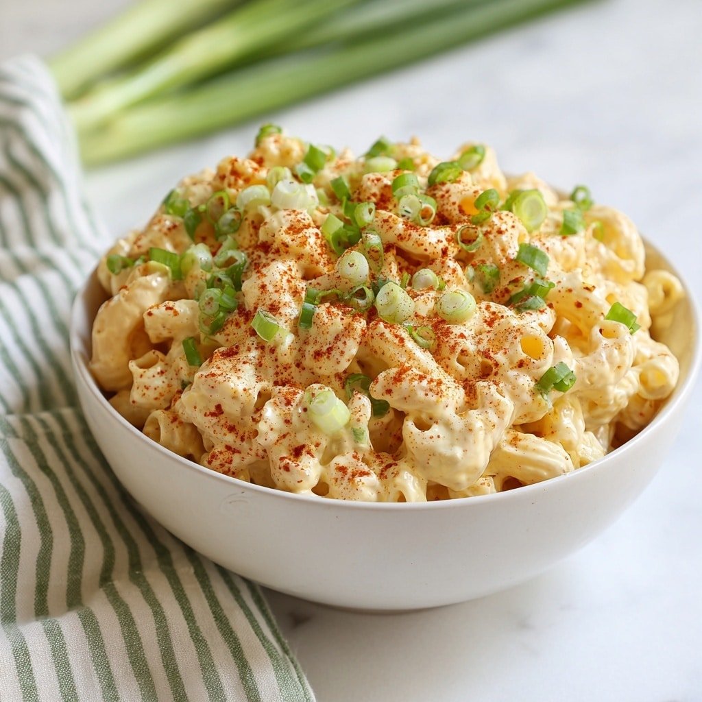 A clear glass bowl shows separate layers of ingredients. On the left side, there is a large pile of chopped hard-boiled eggs with bright yellow yolks and white edges. Next to it, shaped pasta with pale beige color sits near a heap of small chopped green pickles. Below the pickles are small pieces of purple-red onion. In the center of the bowl, there are powders of dark brown spice and a smaller pile of light brown spice. A dollop of creamy pale yellow mustard and a thick white mayonnaise-like sauce are placed near the spices, creating different textures and colors. The bowl is placed on a white marbled surface. Photo taken with an iphone --ar 1:1 --v 7 — Creamy Deviled Egg Pasta Salad, deviled egg pasta salad, easy pasta salad recipes, quick picnic salads, flavorful pasta salad ideas