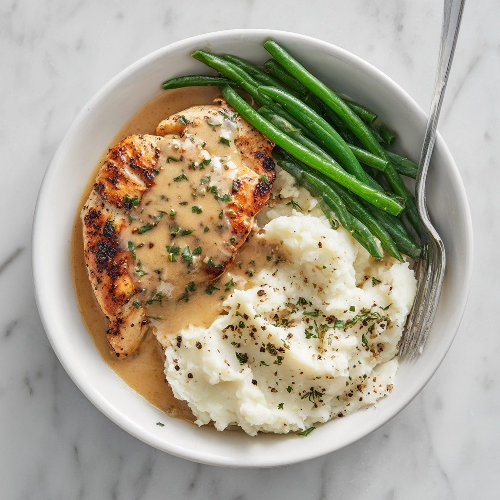The image shows a white enamel pot filled with creamy light brown sauce covering three browned chicken pieces with a slightly crispy texture. The chicken sits in the sauce with some whole peeled garlic cloves scattered around. Small green herb bits are sprinkled on top, adding fresh color. A metal spoon is resting in the pot, partly submerged in the smooth sauce. The pot is placed on a white marbled surface, with a white cloth and some garlic bulbs in the background. photo taken with an iphone --ar 1:1 --v 7 — Creamy Garlic Chicken, Creamy Garlic Chicken Recipe, Easy Creamy Chicken Dinner, Comforting Chicken Recipes, Garlic Chicken with Cream Sauce